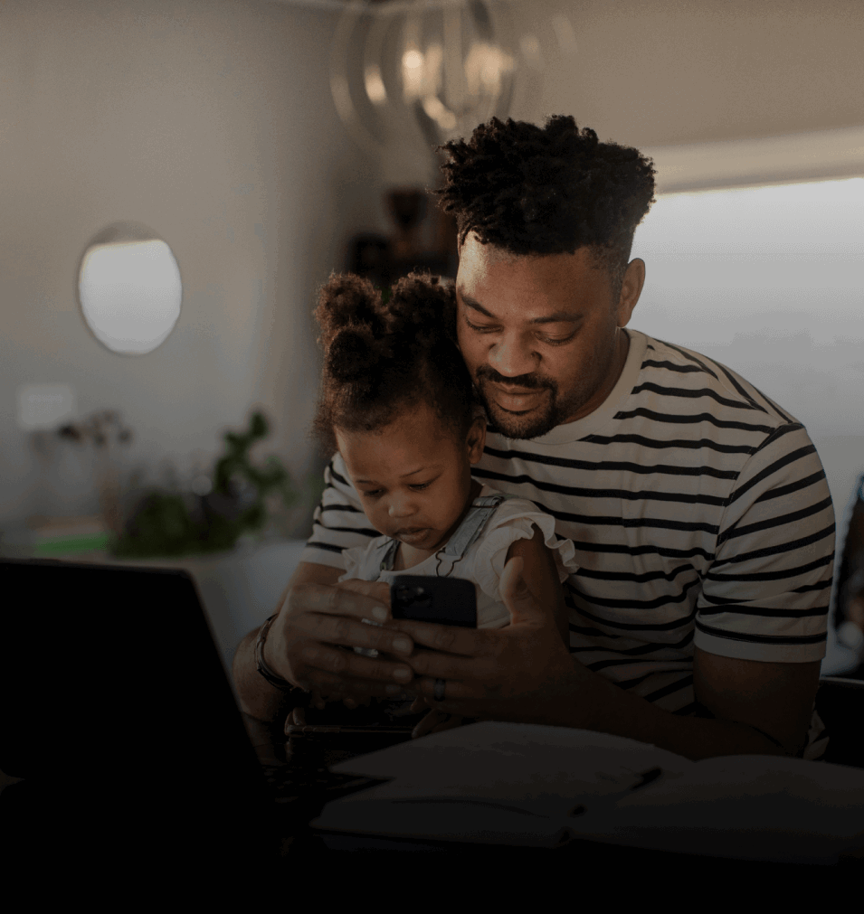 Father & young daughter sat at a desk looking at a smartphone