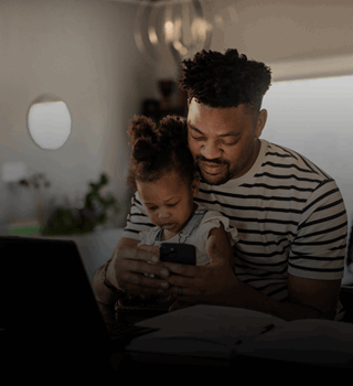 Father & young daughter sat at a desk looking at a smartphone