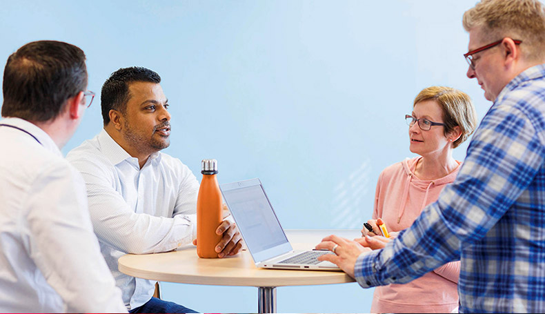 Four colleagues stood chatting around a pedestal table in the office