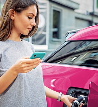 Female holding a smartphone while she charges her electric car